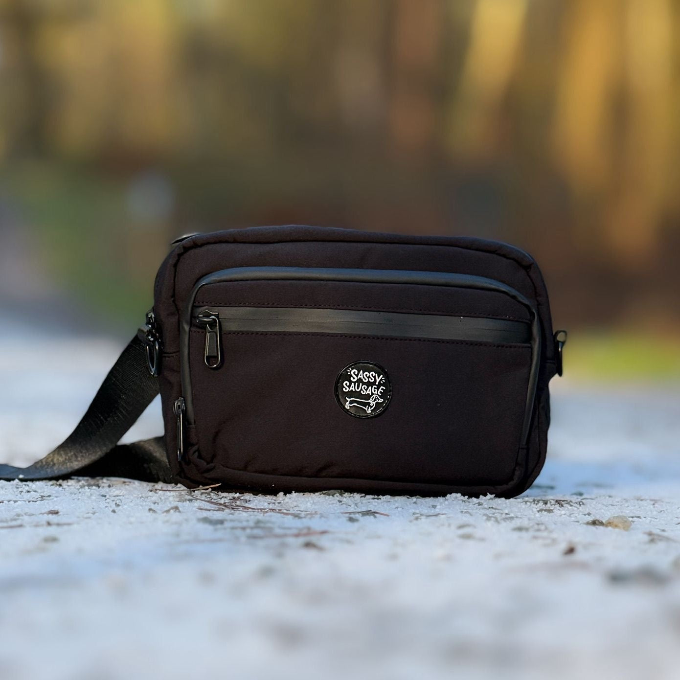 Black crossbody bag on a textured surface with blurred natural background