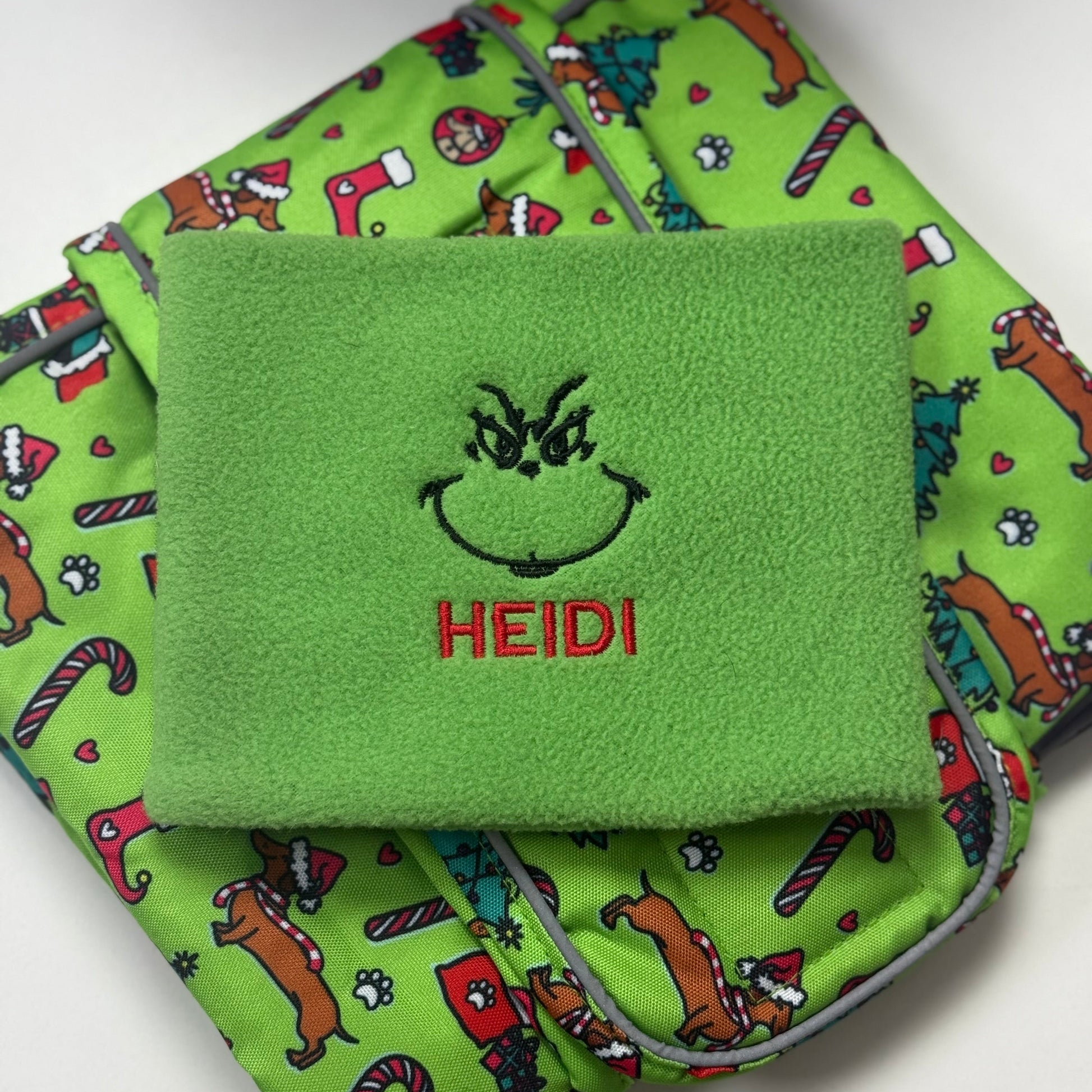 Green fabric with a pattern of cartoon dogs and the name 'HEIDI' embroidered on it.