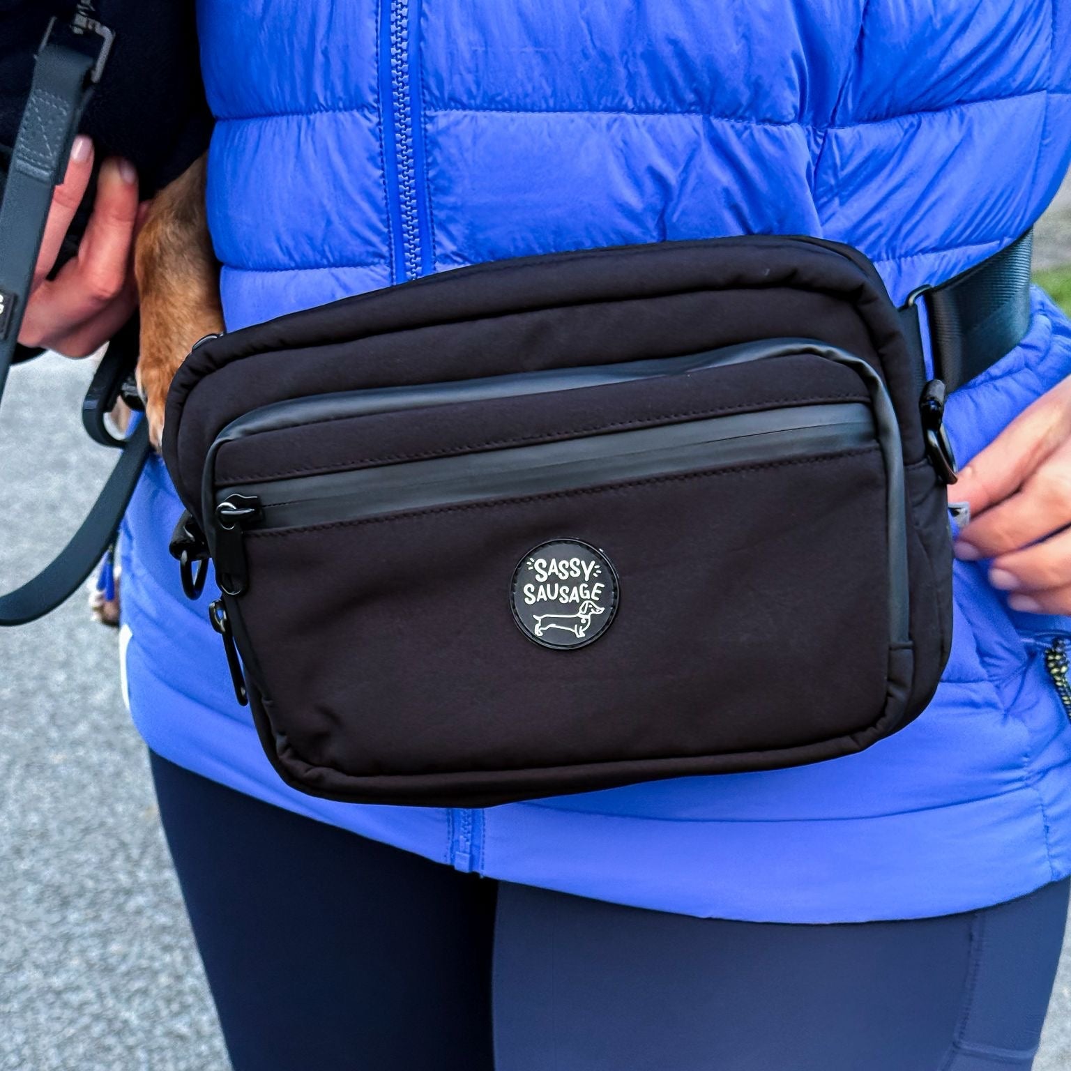 Person wearing a black bag with a visible brand logo, standing on a road.