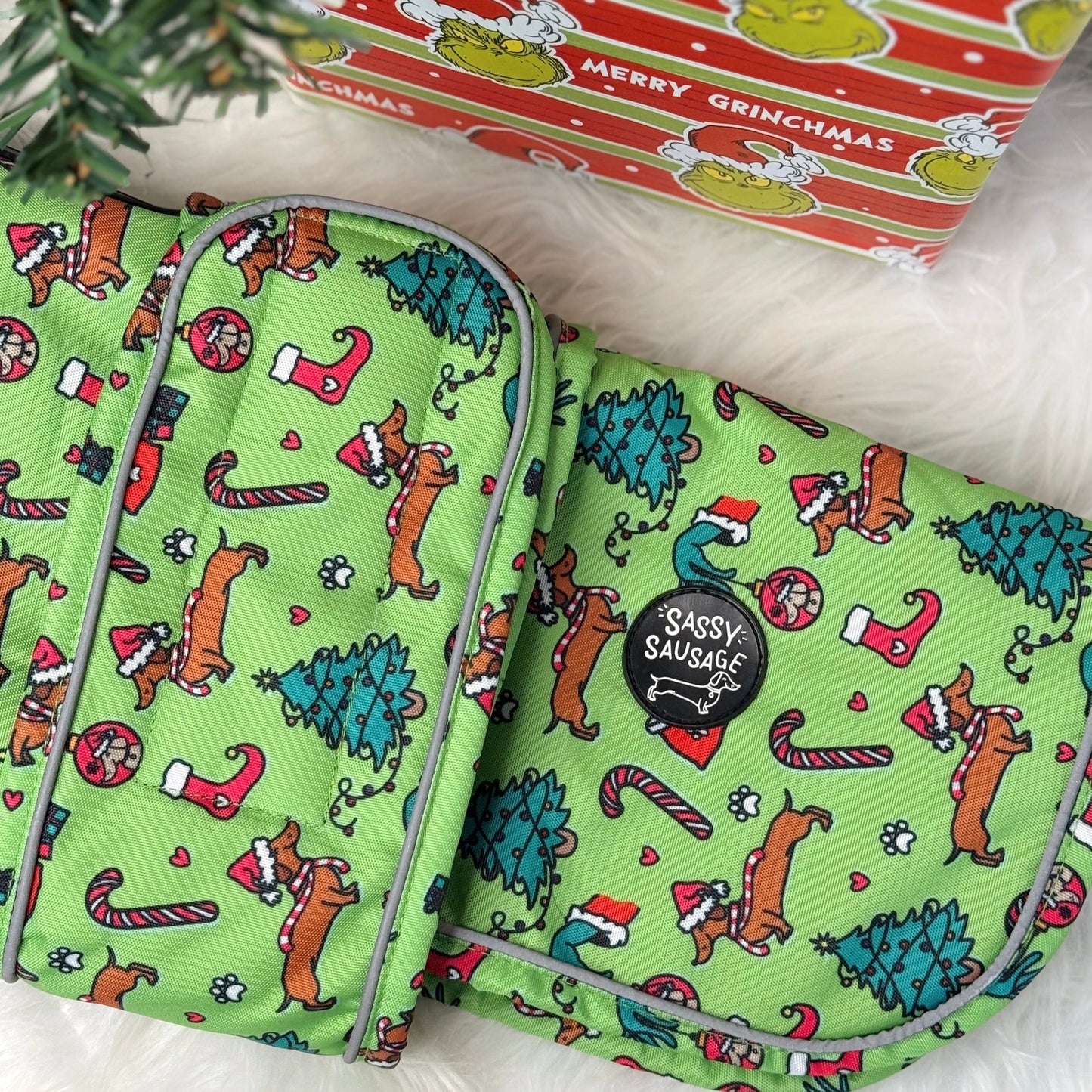 Green patterned product with 'Sassy Sausage' logo next to a 'Merry Grinchmas' box.